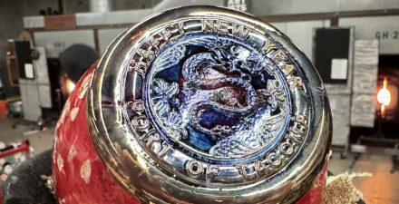 Red glass orb, stamped with a dragon motif, with the Hilltop Artists' hotshop in the background.