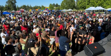Crowd of thousands of attendees at Juneteenth event, listening to music performance on stage.