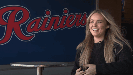 Rylee Pay New Tacoma Rainiers Broadcaster next to banner of Rainiers