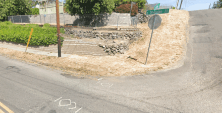 Street view on Sheridan Avenue at South 64th Street showing street name signs, deteriorating asphalt, and missing sidewalk/curb ramp