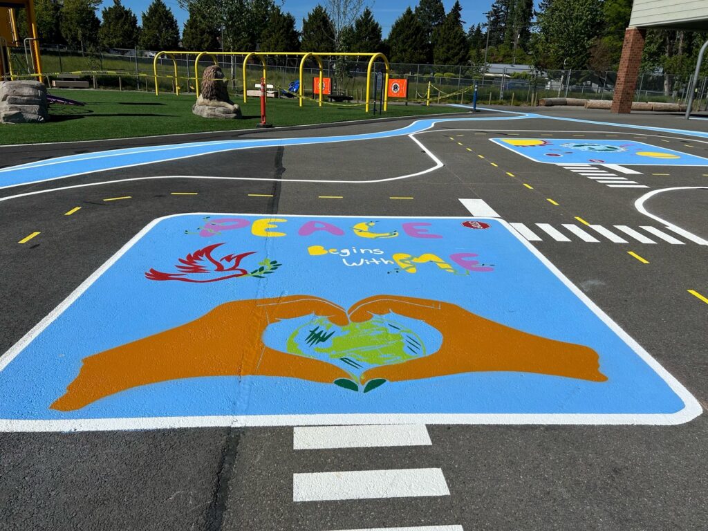 Permanent traffic garden at Stafford Elementary School, featuring white crosswalks and blue decorative elements, with student artwork in the middle.
